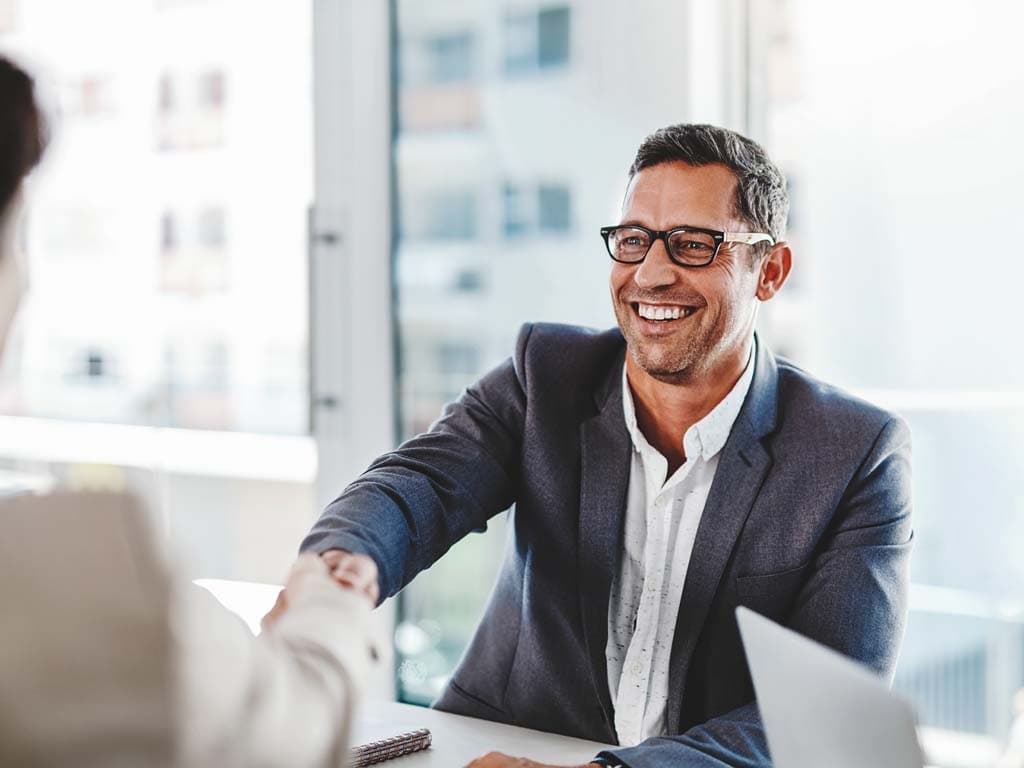 Мъж в костюм се ръкува с жена, символизирайки професионално споразумение или поздрав