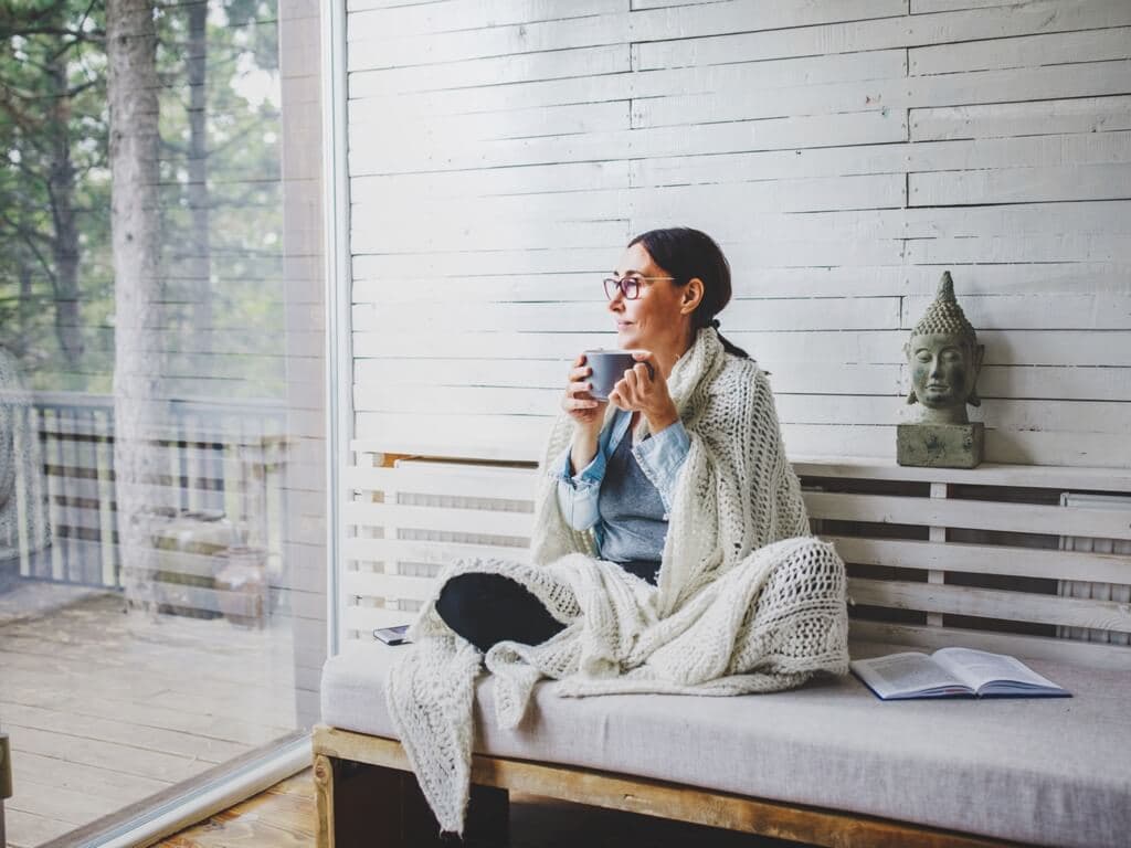 Жена седи на пейка и се наслаждава на чаша кафе в спокойно открито пространство