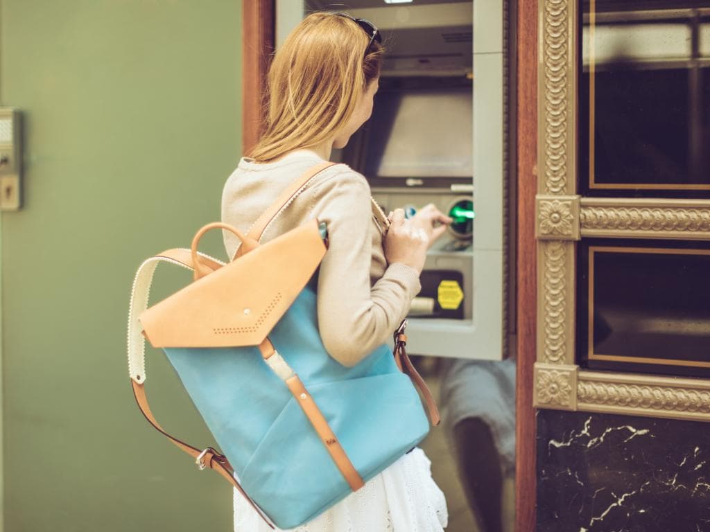 Жена с син раница стои пред банкомат, готвейки се да изтегли пари в брой