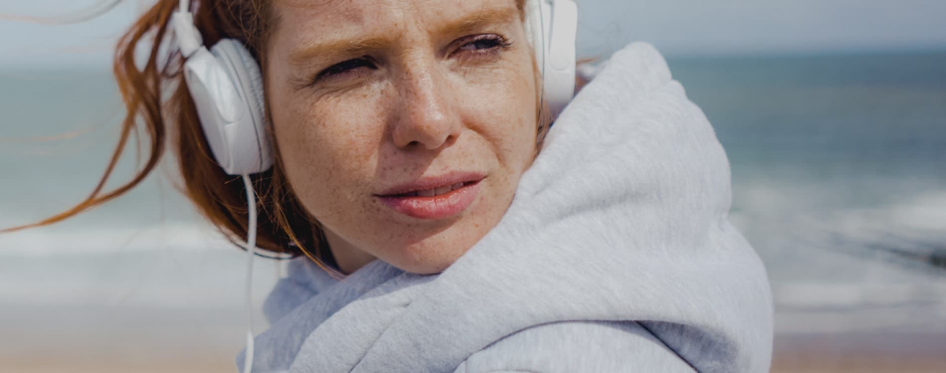 Жена със слушалки се отпуска на плажа, наслаждавайки се на слънцето и звука на вълните